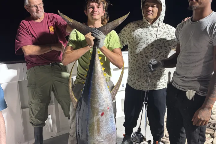 Four people on a boat holding a large fish at night.