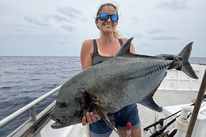 Person on boat holding a large fish with ocean in the background.