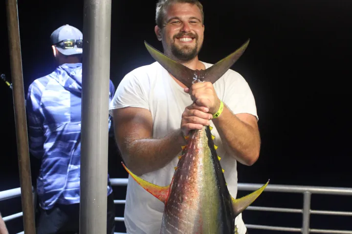 Man on a boat at night holding a large fish, smiling.
