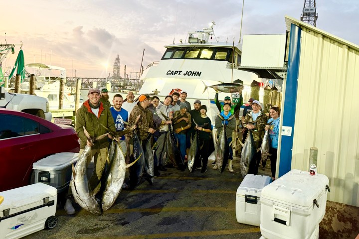 Group of people holding large fish in front of a boat named 'Capt. John' at a dock.